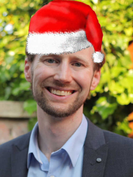 Matt Voight smiles at the camera. And image of a red Santa hat has been superimposed on his head.